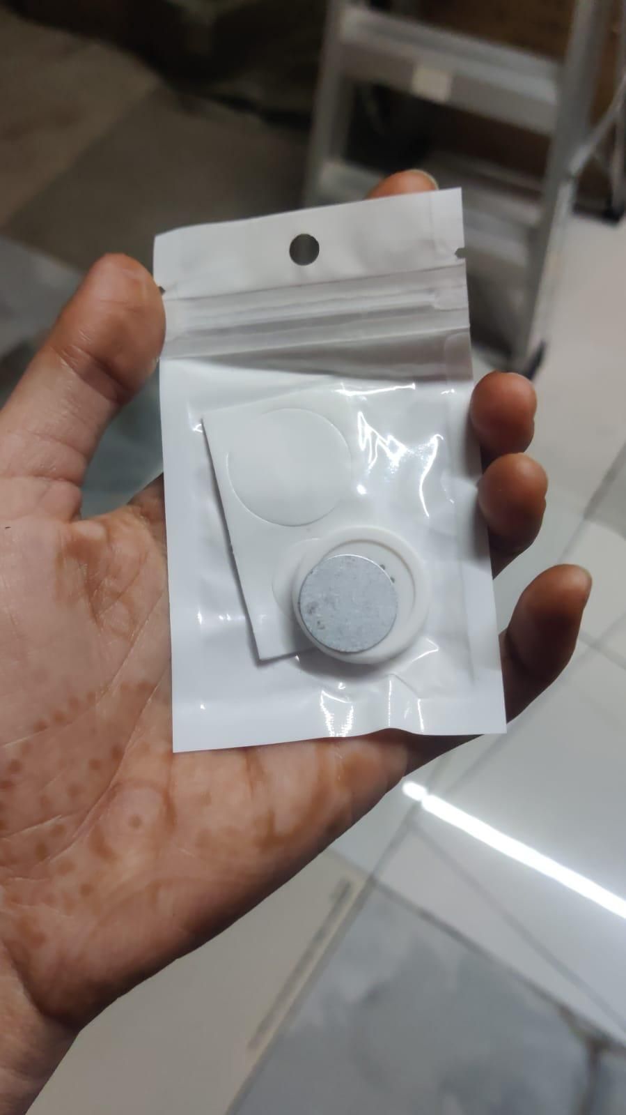 Small round object in a clear plastic packaging held in a hand.