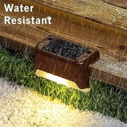 Water-resistant solar light attached to a wooden deck with water droplets.